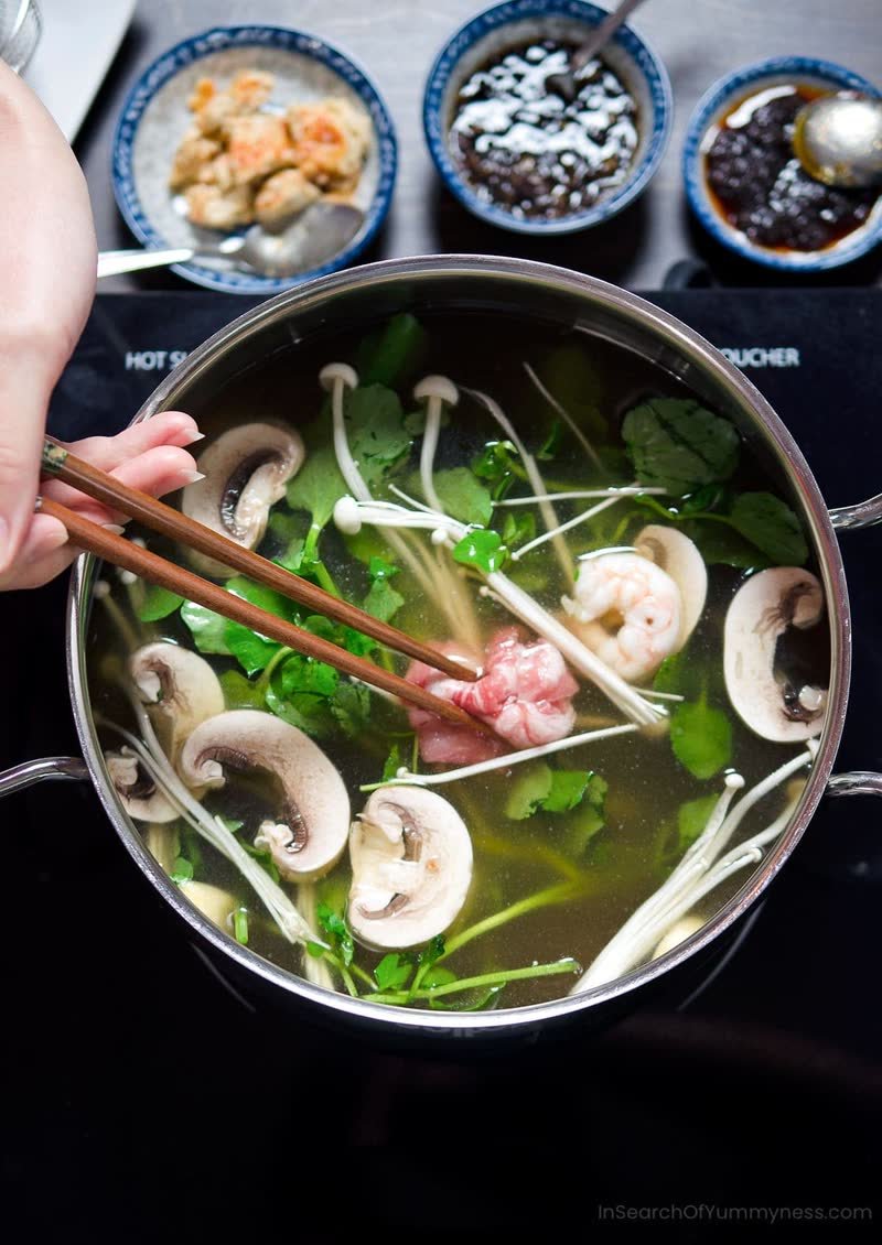 Clear broth with mushrooms and greens being lifted with chopsticks
