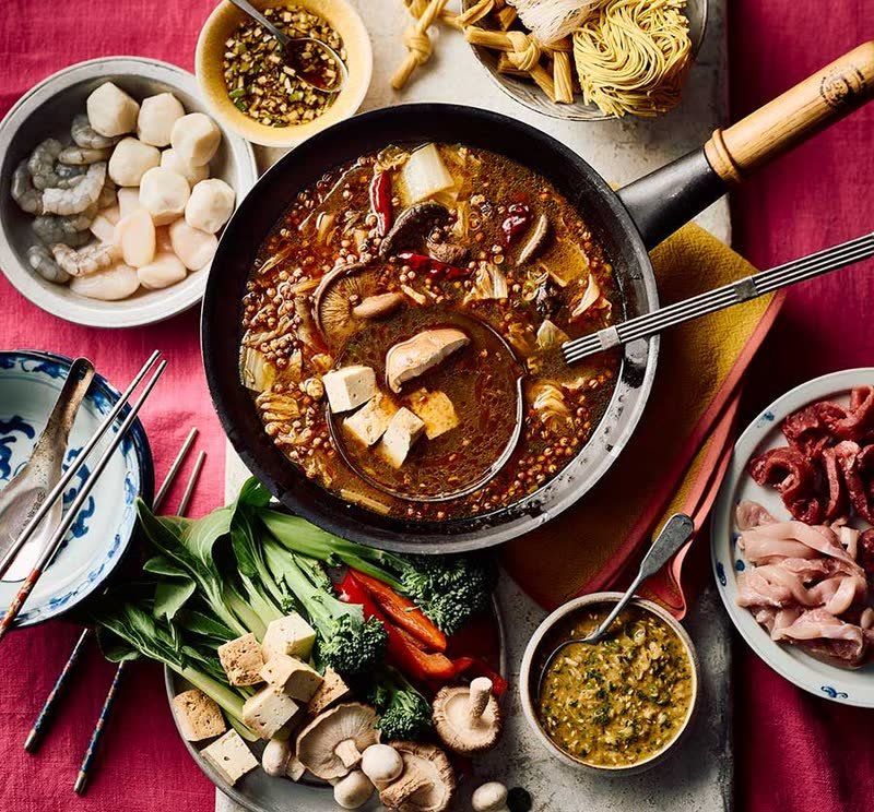Spicy hot pot broth surrounded by shrimp, tofu, greens, mushrooms and sliced meats